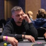 Ein Mann spielt Poker an einem Tisch in einem Casino, umgeben von anderen Spielern und Chips.