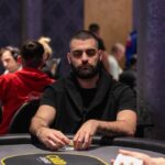 Ein Mann und eine Frau sitzen an einem Pokertisch und spielen eine Partie Poker. Der Mann hält Karten in der Hand, während die Frau konzentriert auf ihre Karten schaut. Im Hintergrund sind Pokerch