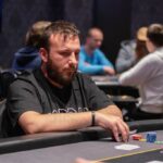 Ein professioneller Pokertisch mit grünem Filz, umgeben von vier Stühlen und einer Deckenbeleuchtung. Auf dem Tisch liegen Pokerchips, Spielkarten und Getränke. Im H