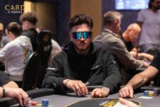 Ein Tisch mit einem Poker-Set, bestehend aus Karten, Pokerchips und Getränken, umgeben von vier Personen, die intensiv Poker spielen.