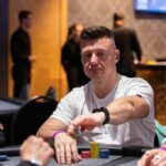 Ein buntes Pokerspiel mit Spielkarten und Chips auf einem grünen Filztisch. Ein Spieler hält seine Karten und setzt Chips in die Mitte des Tisches. Andere Spieler sind im Hintergrund zu sehen