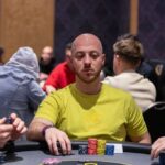 Ein Mann spielt Poker an einem Tisch in einem Casino, umgeben von anderen Spielern und Chips.