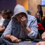 Ein professioneller Pokertisch mit grünen Filz und Pokerchips, umgeben von Spielern mit Karten in der Hand und konzentrierten Gesichtsausdrücken während eines Pokerspiels.