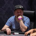 Ein Mann und eine Frau sitzen an einem Pokertisch und spielen Karten. Der Mann hat eine Hand mit Chips und schaut konzentriert auf seine Karten, während die Frau lächelnd ihre Hand betrachtet. Das