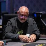 Ein Mann und eine Frau sitzen an einem Pokertisch und spielen Texas Hold'em. Der Mann hat eine Hand aus Karten, während die Frau nachdenklich ihre Karten betrachtet. Im Hintergrund sind Pokerchips und