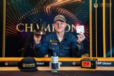 Ein Mann in einem dunklen Anzug und mit kurzem Haar sitzt an einem Pokertisch, umgeben von Spielkarten und Pokerchips. Er schaut konzentriert auf seine Karten und hat eine ernste Mi