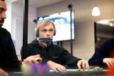 Ein Mann namens Leon Sturm sitzt an einem Pokertisch und konzentriert sich auf sein Blatt Karten, während er eine Sonnenbrille trägt.