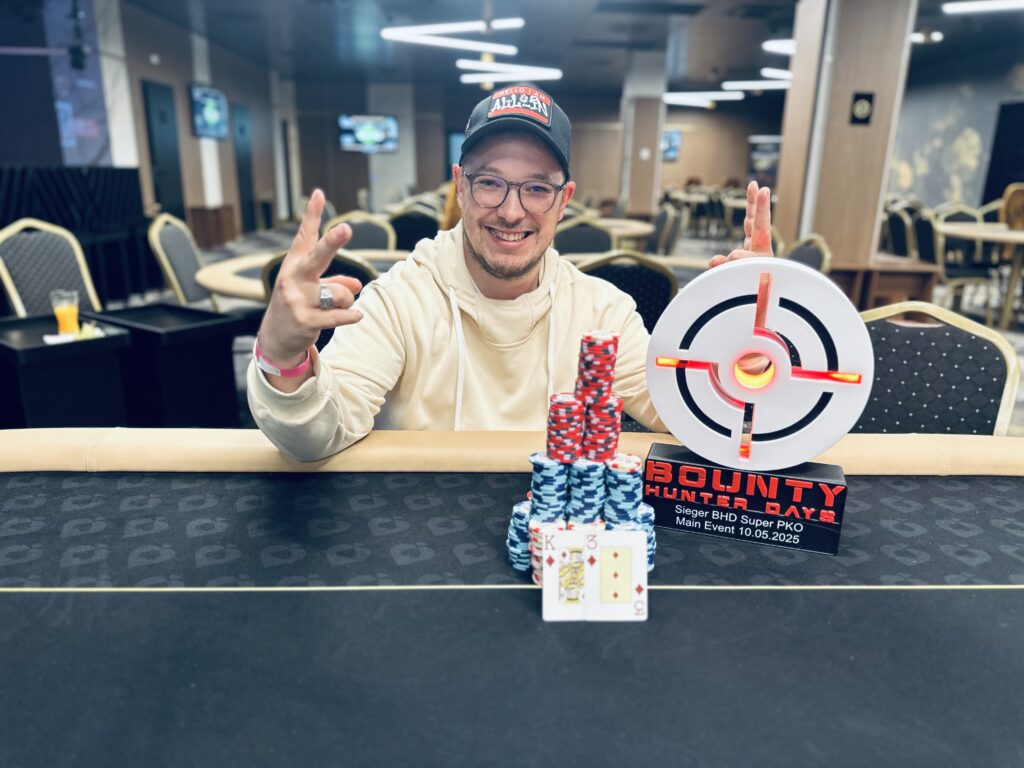 Ein Mann und eine Frau spielen Poker an einem Tisch in einem eleganten Casino. Der Mann hat eine Hand mit Karten, während die Frau konzentriert auf ihre Karten schaut. Hinter ihnen sind andere Spieler und eine Dealerin