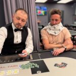 Ein Mann spielt Poker an einem Tisch in einem Casino, umgeben von anderen Spielern. Er hält Karten in der Hand und setzt Pokerchips.