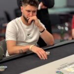 Ein Mann spielt Poker an einem Tisch in einem Casino, umgeben von anderen Spielern und Karten.