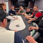Ein Mann spielt Poker an einem Tisch mit grünem Filz. Er hält Karten in der Hand und betrachtet konzentriert seine Chips. Andere Spieler und Glücksspielutensilien sind im H