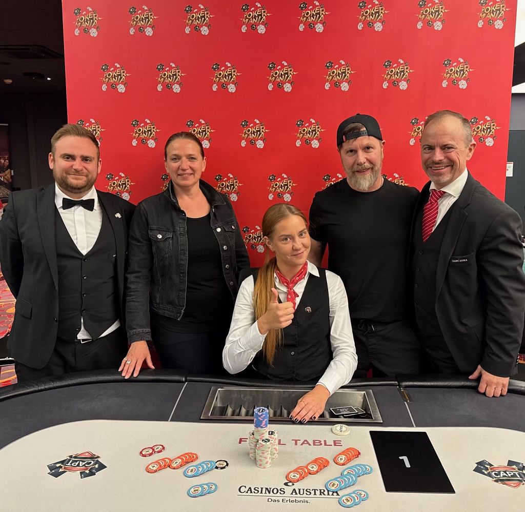 Ein Mann in einem dunklen Anzug sitzt an einem Pokertisch und hält seine Karten in der Hand, während er konzentriert auf die Spielaktionen schaut.