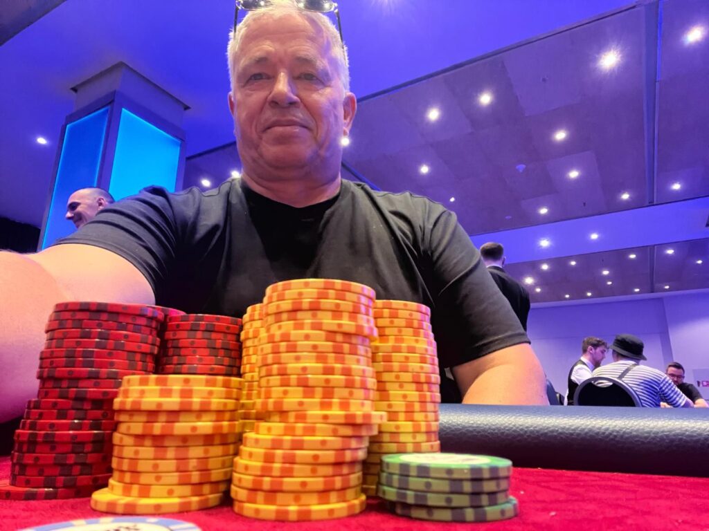Ein Tisch mit einem Kartenspiel, Pokerchips und Getränken, umgeben von vier Personen, die konzentriert Poker spielen.
