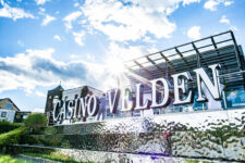 Ein elegantes Casino-Innendesign mit funkelnden Kronleuchtern, roten Teppichen und Spieltischen, umgeben von stilvollen Sitzgelegenheiten und einer glamourösen Atmosphäre.