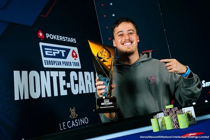 Ein Mann sitzt an einem Pokertisch in einem Casino und hält seine Karten. Im Hintergrund sind andere Spieler und Dealer zu sehen.