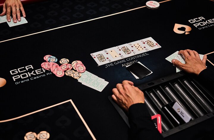 Ein Poker-Tisch mit Spielkarten, Chips und Getränken, umgeben von mehreren Personen, die konzentriert spielen.