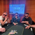 Ein lebendiges Pokerspiel mit fünf Personen an einem Tisch, die Karten halten und konzentriert auf ihre Hände schauen. Die Spieler sitzen um einen grünen Filz-Tisch herum, auf