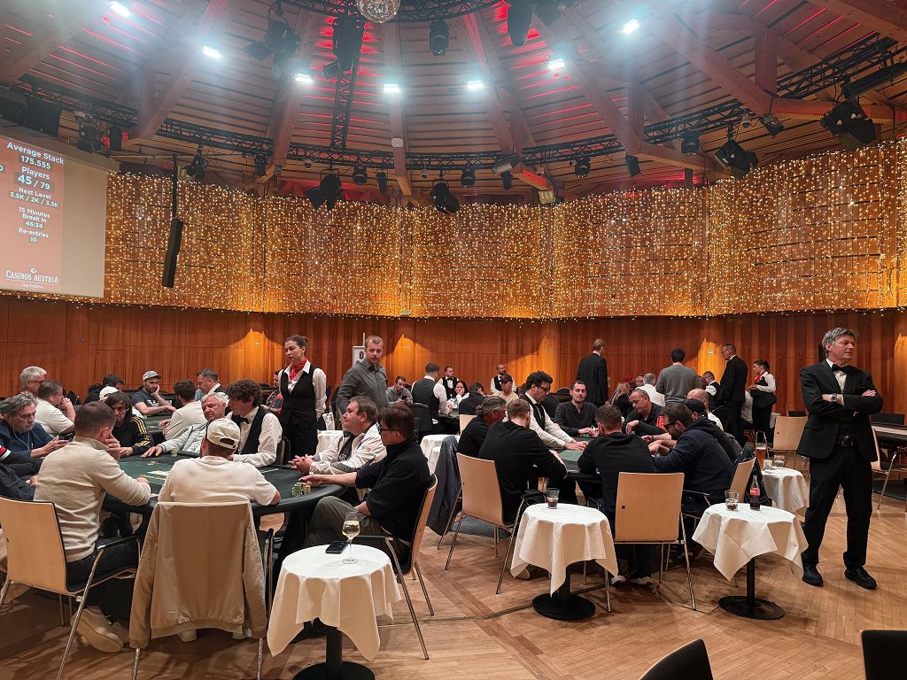 Ein Mann und eine Frau spielen Poker in einem eleganten Casino. Der Mann hat einen Anzug an und die Frau trägt ein rotes Abendkleid. Sie haben Pokerchips vor sich liegen und konzentrieren sich auf ihre