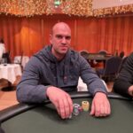 Ein Mann und eine Frau sitzen an einem Pokertisch und schauen konzentriert auf ihre Karten. Um sie herum stehen Chips und Getränke.