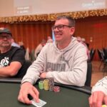 Ein Mann und eine Frau sitzen an einem Pokertisch und spielen Texas Hold'em. Der Mann hat eine ernste Miene, während die Frau lächelt. Karten und Chips liegen auf dem Tisch.