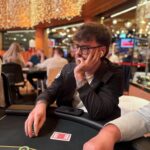 Ein professionell aussehender Pokertisch mit grünem Filz, umgeben von Stühlen, auf denen Spielkarten und Pokerchips liegen. In der Mitte des Tisches sind verschiedene Karten und Jetons