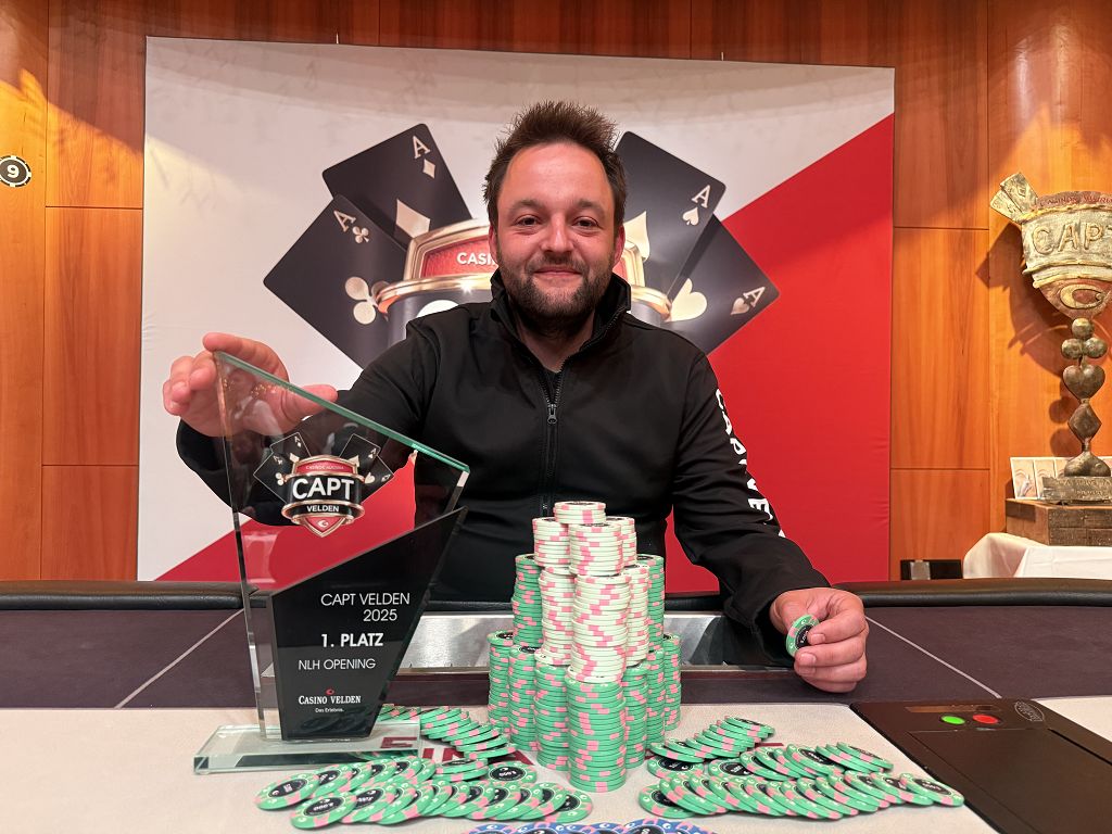 Ein professioneller Pokerspieler mit Sonnenbrille und Kappe, der konzentriert an einem Pokertisch sitzt und seine Karten betrachtet. Im Hintergrund sind weitere Spieler und Pokerchips zu sehen.