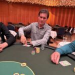 Ein Foto von vier Personen, die am Pokertisch sitzen und Karten spielen. Zwei Männer und zwei Frauen konzentrieren sich auf ihre Karten und Chips. Die Atmosphäre ist gesellig und die Spieler wirken gespan