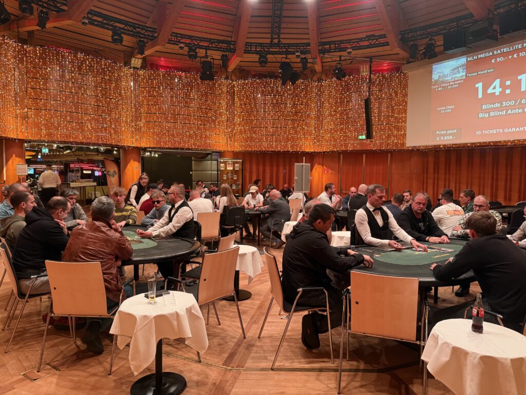 Ein Bild von vier Personen, die an einem Pokertisch sitzen und Karten spielen. Die Personen haben konzentrierte Gesichtsausdrücke und halten ihre Karten fest in den Händen. Ein Stapel Pokerch