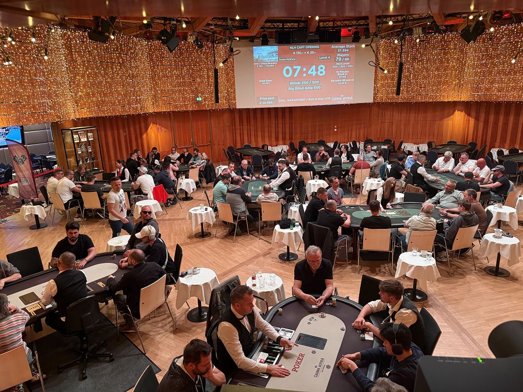 Ein Foto von vier Freunden, die beim Pokern an einem Tisch sitzen und Karten halten. Sie lächeln und haben Spaß.