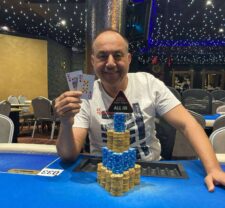 Ein Mann in einem dunklen Anzug und weißem Hemd sitzt an einem Pokertisch und hält Karten in der Hand, während er intensiv auf seine Gegner schaut.