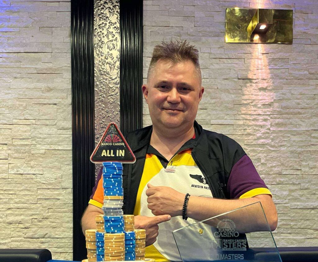 Ein Mann sitzt an einem Pokertisch und hält zwei Spielkarten in der Hand, während er konzentriert auf seine Gegner blickt.