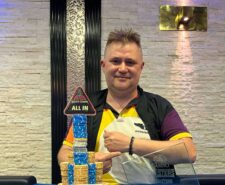Ein Mann sitzt an einem Pokertisch und hält zwei Spielkarten in der Hand, während er konzentriert auf seine Gegner blickt.