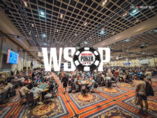 Ein Mann sitzt an einem Pokertisch während eines Turniers der World Series of Poker. Er hat eine Hand mit Karten in der Luft und konzentriert sich auf das Spielgeschehen.