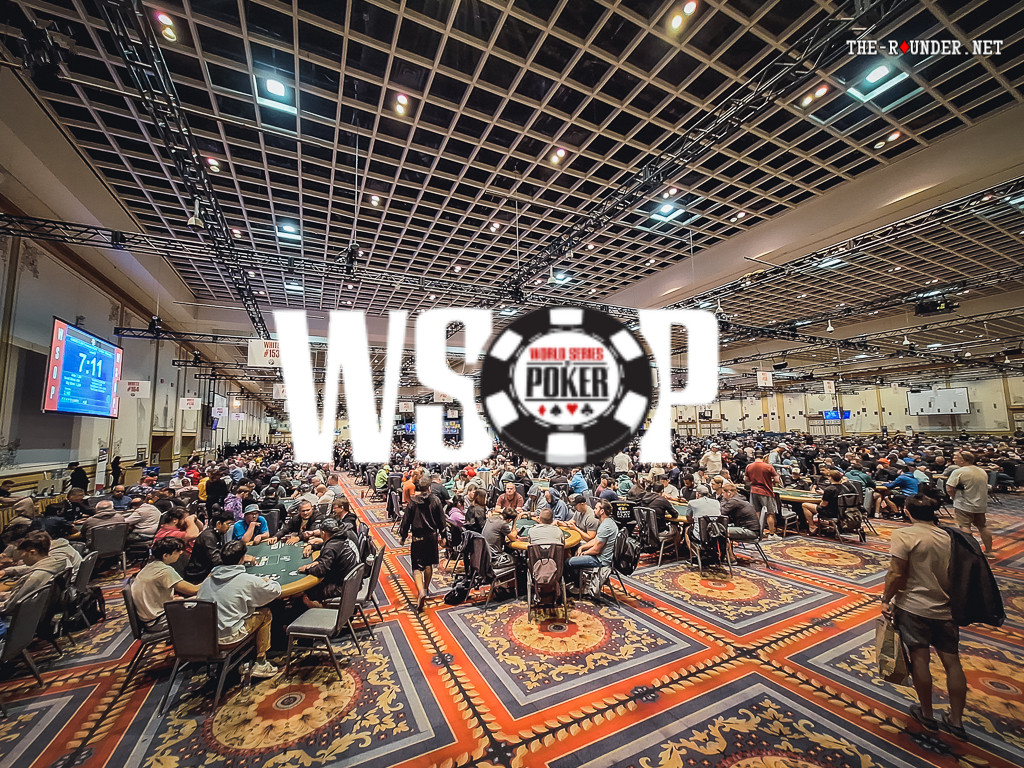 Ein Mann sitzt an einem Pokertisch während eines Turniers der World Series of Poker. Er hat eine Hand mit Karten in der Luft und konzentriert sich auf das Spielgeschehen.