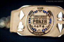 Ein professioneller Pokertisch mit grünen Filz, umgeben von schwarzen Lederstühlen. In der Mitte des Tisches liegen Pokerchips und Spielkarten. Im Hintergrund sind Spieler in gedä