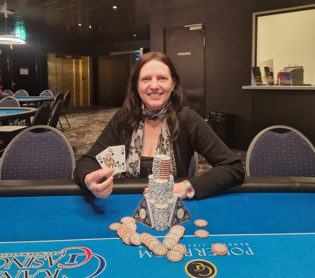 Ein Mann sitzt an einem Pokertisch und hält seine Karten in der Hand, während er konzentriert auf den Tisch schaut. Im Hintergrund sind Casino-Chips und andere Spieler zu sehen.