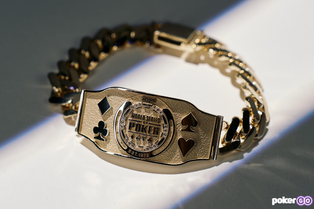Ein Mann in einem schwarzen Anzug und einer Sonnenbrille hält stolz ein goldenes Armband in die Luft, umgeben von jubelnden Menschen in einem Casino. Es scheint, als hätte er gerade ein
