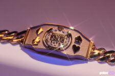 Ein Mann sitzt an einem Pokertisch und hält stolz ein goldenes Armband in die Luft. Er ist von anderen Pokerspielern umgeben und feiert seinen Sieg bei der World Series of Poker.