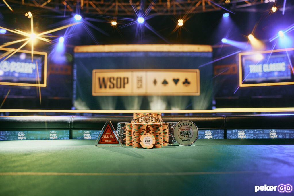 Ein Spieler mit einer Sonnenbrille trägt stolz ein glänzendes goldenes Armband, das ihn als Gewinner der World Series of Poker 2025 kennzeichnet. Im Hintergrund sind jubelnde Menschen zu
