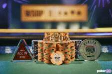Ein Mann in einem schwarzen Anzug feiert mit einem goldenen Armband in der Hand. Er steht vor einem Hintergrund mit Pokerchips und spielt wahrscheinlich bei der World Series of Poker.
