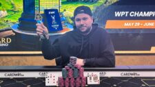 Ein professioneller Pokerspieler sitzt an einem Tisch mit Chips und Karten, während er konzentriert auf seine Hand schaut. Im Hintergrund sind andere Spieler und eine Dealerin zu sehen.