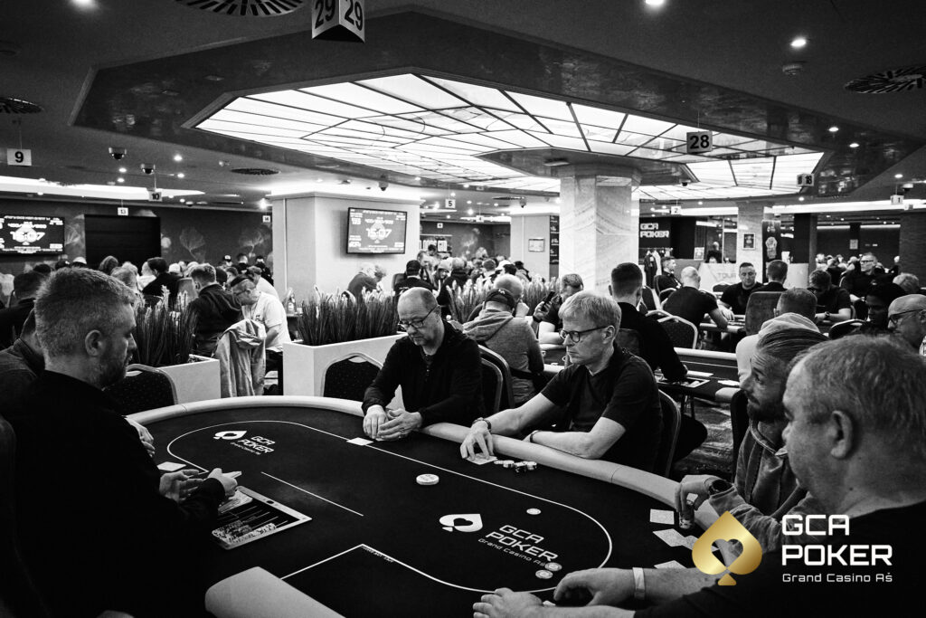 Ein lebendiges Pokerturnier mit einer Gruppe von Spielern, die um einen Tisch sitzen und Karten halten. Die Spieler sind konzentriert und fokussiert, während sie ihre Chips stapeln und ihre H