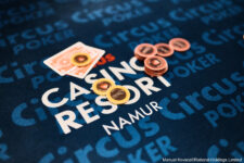 Ein Mann spielt Poker an einem Tisch in einem Casino, umgeben von anderen Spielern und einer Mischmaschine für Karten.