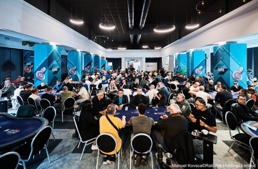 Ein Mann sitzt an einem Pokertisch und betrachtet seine Karten konzentriert, während er von anderen Spielern umgeben ist. Die Spannung und Intensität des Pokerspiels sind spürbar.