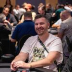 Ein Mann spielt Poker an einem Tisch mit grünen Filz und Chips. Er hat eine Kartenhand und konzentriert sich auf das Spiel.