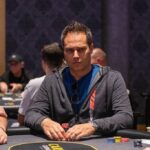 Ein Mann und eine Frau sitzen am Pokertisch und halten ihre Karten. Sie sind konzentriert und haben Pokerchips vor sich liegen.