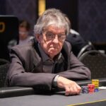 Ein Mann und eine Frau sitzen an einem Pokertisch und halten Karten in der Hand. Sie schauen konzentriert auf ihre Karten, während im Hintergrund Pokerchips und Getränke zu sehen sind.