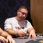 Ein Mann und eine Frau sitzen an einem Pokertisch und betrachten konzentriert ihre Karten. In der Mitte des Tisches liegen Pokerchips und Spielkarten. Die beiden tragen elegante Abendkleid