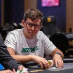 Ein Mann und eine Frau sitzen an einem Pokertisch, halten Karten in den Händen und schauen konzentriert auf den Tisch. Sie sind von Pokerchips und Getränken umgeben.