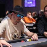 Ein glücklicher Mann sitzt an einem Pokertisch und hält eine Hand mit Spielkarten. Er hat einen konzentrierten Ausdruck im Gesicht und ein Stapel Pokerchips vor sich. Im Hintergrund sind